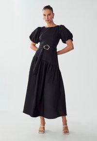 Musta midi mekko kevyessä kankaassa, jossa on lyhyet puffihihat, istuva vartalo ja vyöllä varustettu vyötärö, jossa on kultasävyinen solkiyksityiskohta.