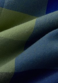 Geweven stof met een chevronpatroon in groen en blauwe tinten. De textuur is glad met een lichte glans, met diagonale lijnen.