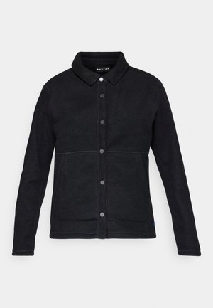 Crna flis jakna s dugmadi sprijeda, oštrim ovratnikom i dva bočna džepa. Ima kontrastne šavove i oznaku s logotipom na rubu.