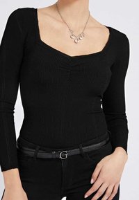 Zwart geribd longsleeve top met een vierkante hals, voorzien van een geplooid detail in het midden. Draagt een zwarte riem met een zilverkleurige gesp.