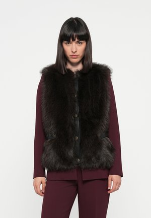 Gilet in finta pelliccia nera con bottoni frontali, tasche laterali e colletto, indossato sopra un top a maniche lunghe borgogna e pantaloni abbinati.