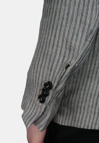 Manica di un blazer a righe in tessuto grigio chiaro e blu navy, con tre bottoni neri e bordi grezzi, che mette in evidenza un design su misura.