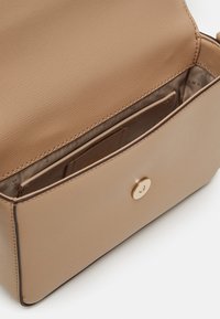 Béžová kožená kabelka s texturovaným povrchem, vybavená zlatým zapínáním na cvok a vnitřní přihrádkou na karty v světlejší látkové podšívce.
