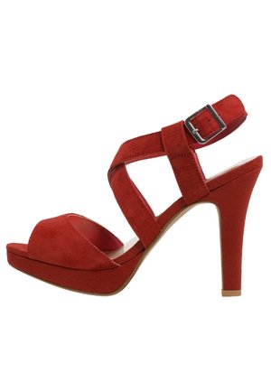 Sandale à talons hauts en daim rouge avec une plateforme, présentant des brides croisées et une boucle sur le côté. Texture lisse et design de talon courbé.