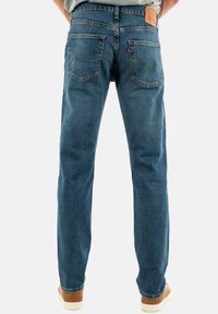 Vaqueros de mezclilla azul con corte recto, que presentan dos bolsillos traseros con detalles de costura y una etiqueta de cuero en la cintura.