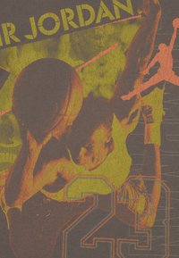 Το γραφικό T-shirt διαθέτει φθαρμένο τύπωμα ενός παίκτη μπάσκετ σε πορτοκαλί και κίτρινο πάνω σε σκούρο φόντο, με τα κείμενα "23" και "Mr. Jordan".