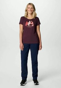 Burgundy t-shirt med kort ärm som har en grafik med träd, björnar och sol. Matchas med marinblå byxor och svarta sneakers.