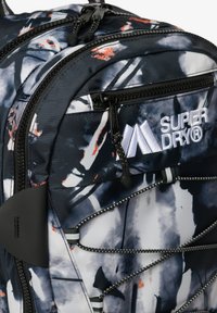 Sac à dos avec une palette de couleurs noire, blanche et marine, doté de motifs abstraits, de doubles zips et d'un cordon élastique à l'avant pour le stockage externe.