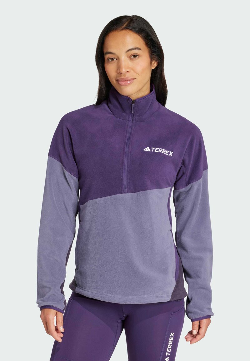 Fleece-pullover i mørk og lys lilla med høy hals, halv glidelås og en hvit logo på brystet. Myk tekstur overalt.