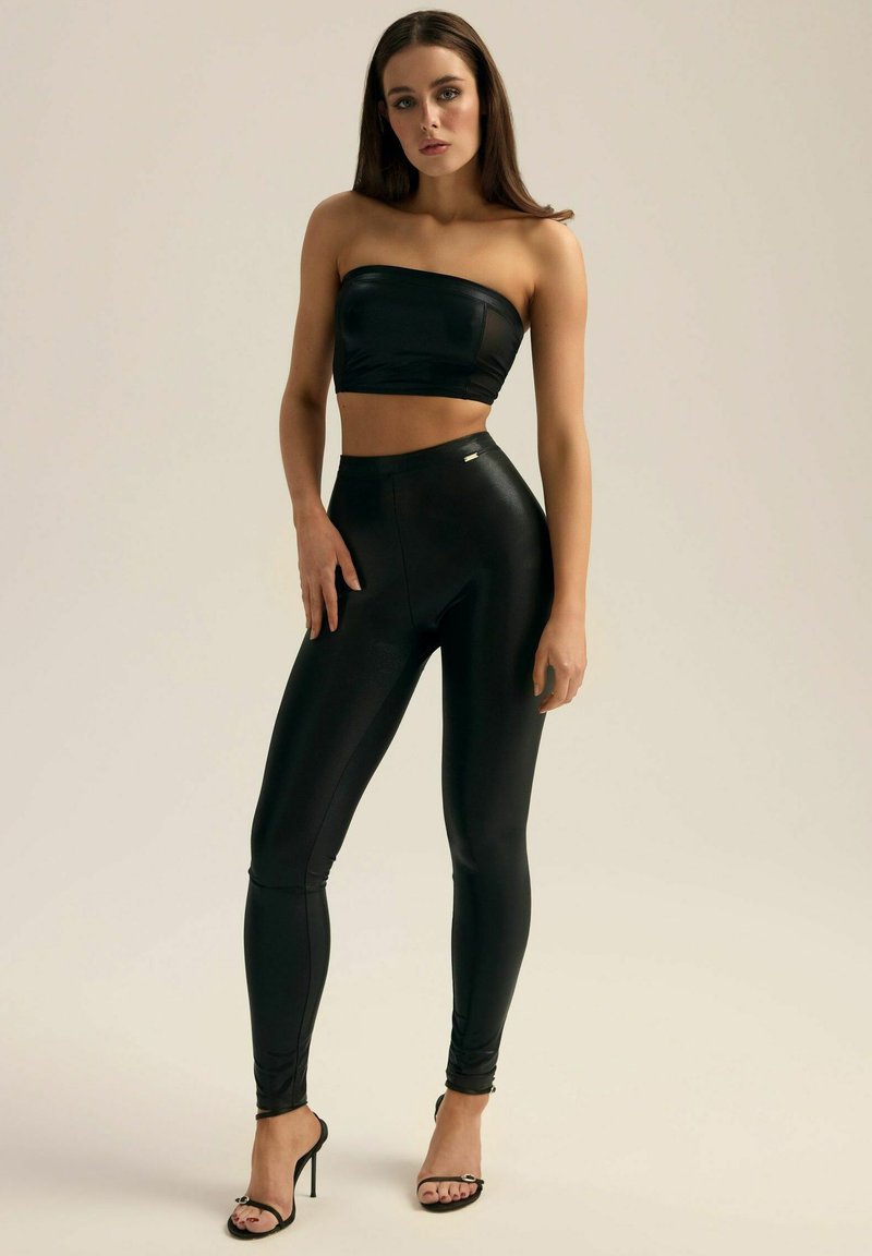 Czarny strapless krótki top w zestawie z wysokimi legginsami, z błyszczącą teksturą i subtelnym detalem brandingowym. Sandały na wysokim obcasie.