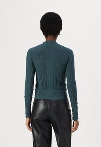 Pull en maille côtelée couleur sarcelle avec manches longues et col rond. Présente une silhouette ajustée et des détails texturés le long du dos et des poignets.