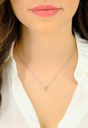 Silberne Anhänger-Halskette mit einem kleinen Zirkonia-Stein. Feine Kette mit verdrehtem Design, getragen über einem weißen Hemd mit Kragen.