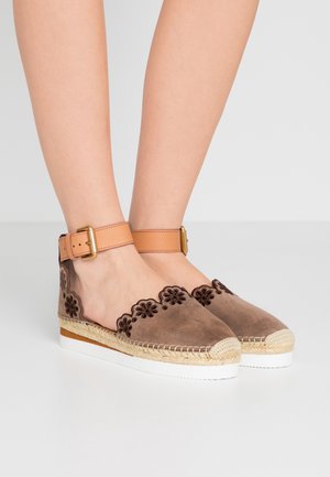 Bruine suède espadrilles met een gegolfde rand, bloemenborduursel en een tan enkellipje. Voorzien van jute details en een witte rubberen zool.