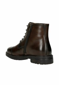Stivaletto in pelle marrone con punta arrotondata, chiusura con lacci sul davanti e zip laterale. Suola texturizzata con un design robusto e chunky.