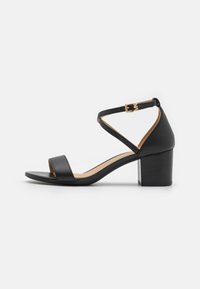 Sandale en cuir noir avec un design à lanières croisées, un bout carré, un petit talon block et un détail de boucle sur la lanière de la cheville.