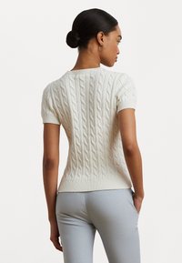 Short-sleeve cable-knit sweater in off-white, featuring a ribbed collar and hem, with a textured, raised pattern throughout.