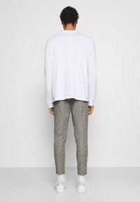 Vit långärmad skjorta med rund halsringning, ihop med grå mönstrade byxor. Modellen bär vita sneakers och ankelsockor.