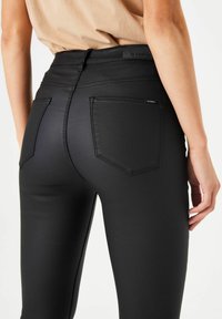 Vaqueros negros de tiro alto, elásticos y con una textura suave. Cuenta con dos bolsillos traseros con costuras negras y una etiqueta de marca sutil en la cinturilla.