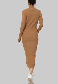 Robe col montant côtelée couleur camel avec des manches longues et une silhouette ajustée, arrivant mi-mollet, associée à des baskets blanches.