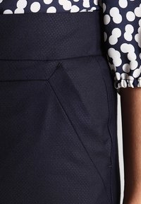 Marinblå kjol med texturerad tyg, åtsittande midjeband och snedställda sidofickor, kombinerad med en mönstrad blus med vita prickar.