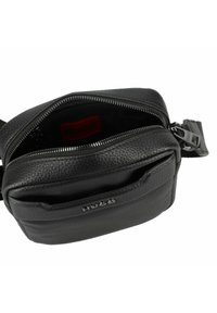 Borsa a tracolla nera in pelle con esterno texture, acchardware in argento, tasca frontale con zip e etichetta interna rossa. Design compatto e rettangolare.