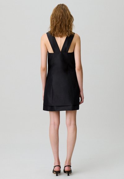 Abito in satin nero con schiena a V e spalline larghe. Caratterizzato da un orlo stratificato, una texture liscia e un design fino al ginocchio.