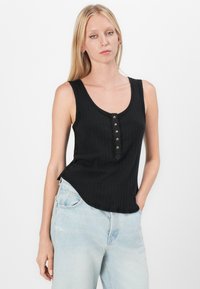 Svart ribbet tanktop med rund hals, med en knappestolpe og sidespalte, parret med lyseblå høyhårete jeans.