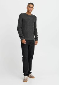Dark grey ribbed knit sweater with a round neckline, paired with black pants and gray-brown sneakers. Smooth texture, fitted design.