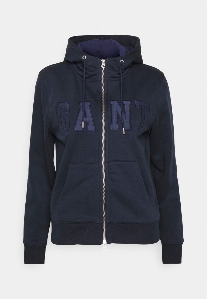 Sudadera con cremallera de color azul marino hecha de tela suave. Presenta una capucha con cordón, bolsillos frontales y un logo bordado de "GANT" en un color a juego.