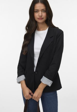 Sort skræddersyet blazer med en enkelt knaplukning, der har stribede manchetter og klapkrave, parret med en hvid t-shirt og blå jeans.