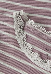 Detailní záběr na proužkovanou ribkovou látku v lila a bílé barvě s bílou krajkou na okraji, na které jsou vidět texturované pletené vzory a švy.
