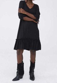 Svart klänning med V-ringning, trekvartsärmar och volangkant. Buren med knähöga svarta cowboystövlar med spetsig tå.