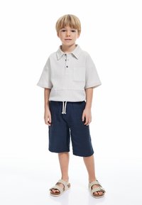 Ljusgrå kortärmad polo med textur och ficka, tillsammans med marinblå shorts med dragsko. Beige sandaler med remmar fulländar looken.