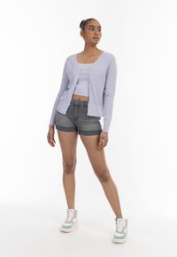 Jasnofioletowy dziergany kardigan z teksturowanym wzorem, z zapięciem na guziki, noszony na dopasowanej bluzce crop top i szarych szortach dżinsowych. Kolorowe sneakersy dopełniają stylizację.