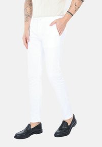 Pantaloni bianchi slim-fit in cotone con una texture liscia, dotati di tasche laterali. Abbinati a mocassini neri per creare un contrasto.