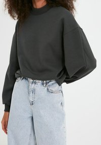 Sudadera de color gris carbón con cuello alto y hombros caídos, combinada con jeans de tiro alto en azul claro con una textura desgastada.