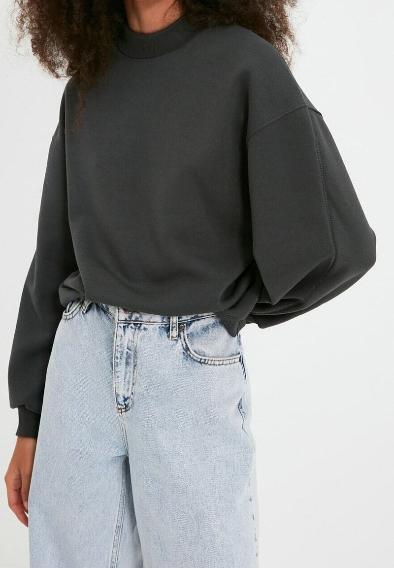 Sudadera de color gris carbón con cuello alto y hombros caídos, combinada con jeans de tiro alto en azul claro con una textura desgastada.