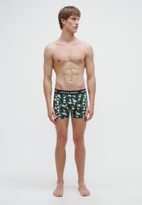 Boxeri cu imprimeu cu frunze verzi și flamingo albi, având o talie elastică neagră inscripționată cu "JACK & JONES". Materialul pare moale și elastic.