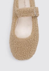 Beige Mary Jane shoe with fluffy textured fabric, a rounded toe, and a silver buckle strap across the foot opening. Soft, cozy appearance.