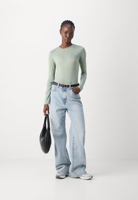 Lys grønn langermet topp, løse blå denimjeans, svart belte, svart håndveske og grå joggesko, som skaper et uformelt antrekk.