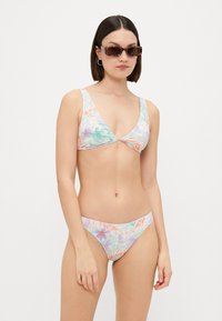 Compleu de bikini floral, cu un top triunghiular și o fundiță jos, în culori pastelate. Țesătură netedă cu un model de frunze tropicale.
