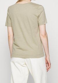 Camiseta de manga corta color caqui con cuello redondo. Tejido de algodón suave, corte ajustado con dobladillo recto y detalles de costura limpios.