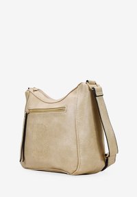 Bolso de mano de cuero sintético beige con textura de gamuza, que cuenta con un bolsillo con cremallera y un diseño de letra "B" tachonada en la parte frontal. Acento de correa negra.