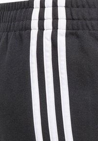Pantalones cortos deportivos negros con un tejido texturizado, cintura elástica y tres franjas verticales blancas a lo largo del lado para dar detalles.