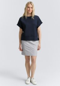 Navy blauw kortmouwen top met een ontspannen pasvorm, gecombineerd met een grijze gestreepte rok. Model draagt witte sneakers en staat op een neutrale achtergrond.
