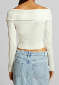 Biała bluzka z odkrytymi ramionami, prążkowana, z długimi rękawami, dopasowana, zestawiona z jasnoniebieską spódnicą dżinsową z tylnymi kieszeniami.