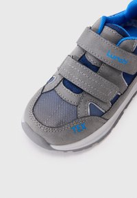 Sive tenisice za sport s plavim akcentima, mrežastim panelima i dva čičak traka. Istaknuta oznaka na strani i teksturirani materijali za bolje prianjanje.