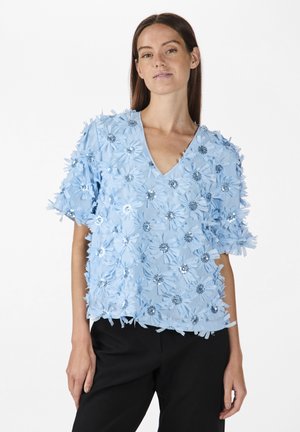 Light blue top with a V-neck, adorned with 3D floral embellishments and sequins, featuring short sleeves and a relaxed fit.