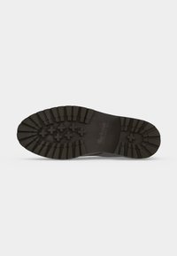 Semelle de chaussure en caoutchouc noir avec des rainures profondes et des motifs en forme de croix, affichant le nom de la marque et une prise texturée pour une utilisation en extérieur.