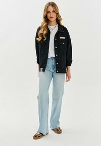 Czarna dżinsowa kurtka z naszywką, biała koszulka, jasnoniebieskie dżinsy w kształcie dzwonów oraz buty slip-on w panterkę. Gładkie, casualowe tekstury materiałów.